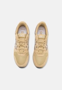 Zapatos deportivos beige con materiales de malla y ante, que presentan un diseño texturizado, cordones y un logotipo en la lengüeta.