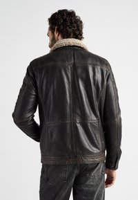 Bruine leren jack met een schapenvacht kraag, met een textuur op het oppervlak en gestikte panelen. Draag het met donkere spijkerbroek.