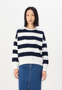 Marinblå och vit randig tröja med rundad halsringning, sänkta axlar och ett mjukt, texturerat tyg. Kombinerad med en denimkjol.