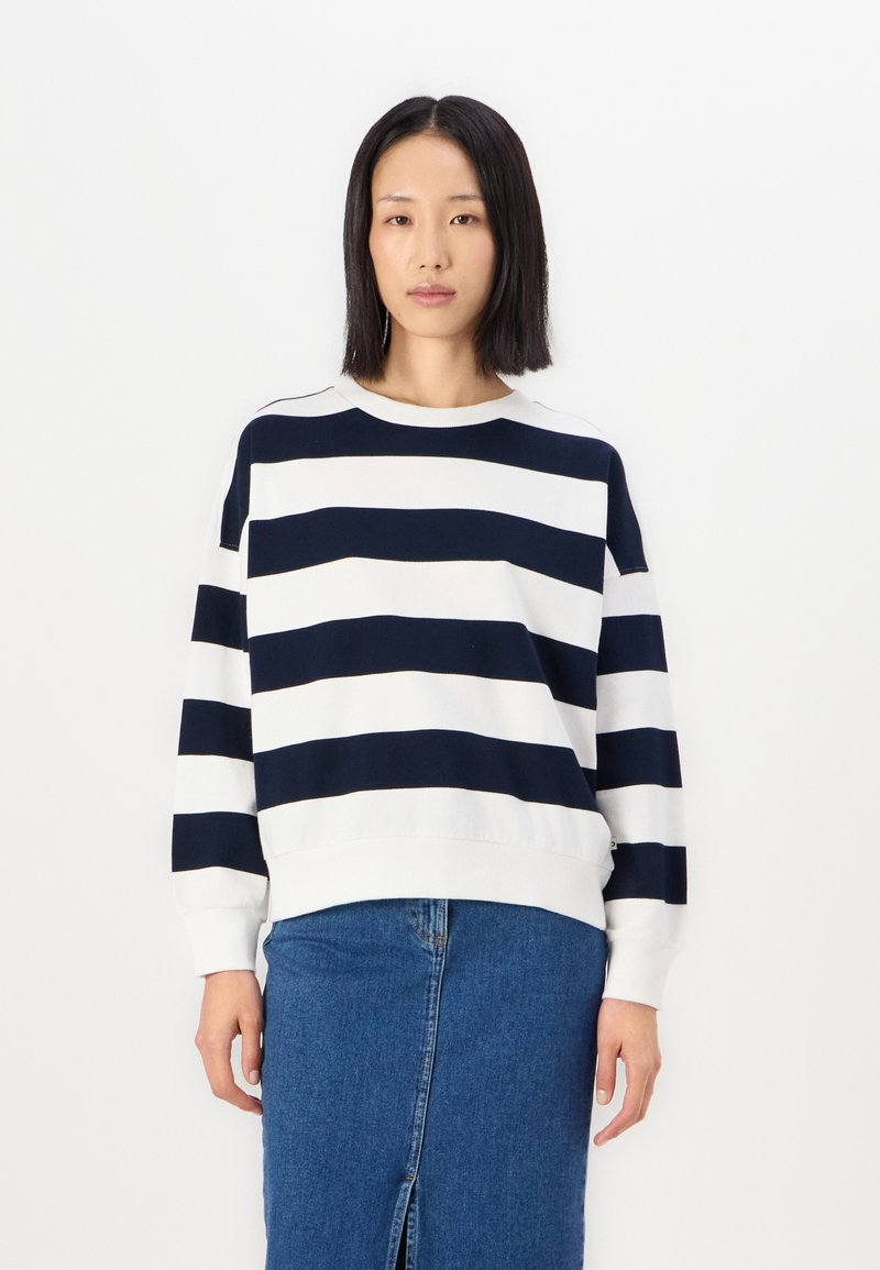 Marinblå och vit randig tröja med rundad halsringning, sänkta axlar och ett mjukt, texturerat tyg. Kombinerad med en denimkjol.