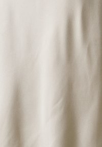 Tissu beige texturé avec un motif de grain subtil et un doux éclat. Le matériau semble léger et lisse, adapté à diverses applications.