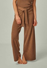 Braune, weit geschnittene Hosen mit Gürtel, aus weichem Textilgewebe, mit Schlitzen an den Seiten für zusätzliche Details.