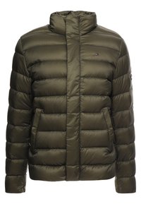 Olivgrön puffjacka med horisontell quiltning, hög krage och dragkedjefickor på sidorna. Har logotyp på övre vänstra bröstet. Slät textur.