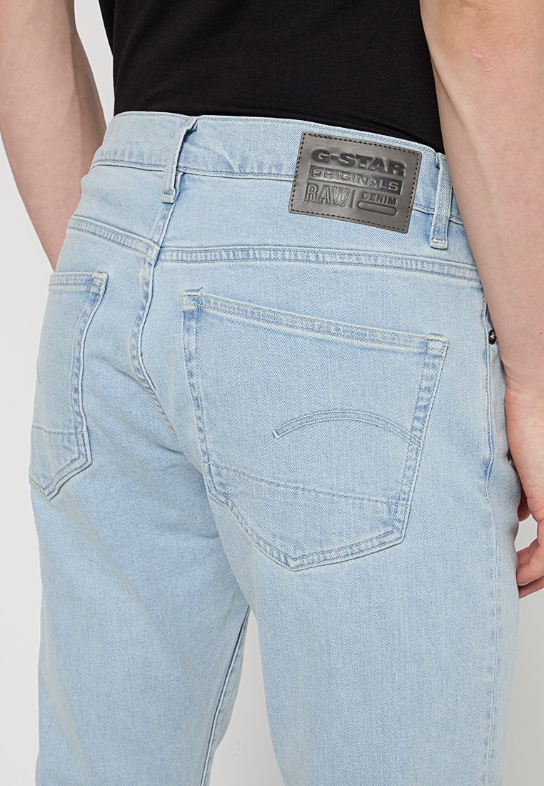 Hellblaue Jeans aus Denim mit Gesäßtaschen und einem schwarzen Lederetikett von G-Star Originals RAW am Bund, kombiniert mit einem schwarzen Oberteil.