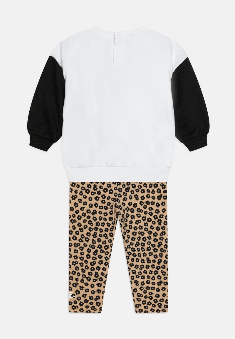 Leichter Sweatshirt in Weiß mit schwarzen Ärmeln; kombiniert mit beigen Leggings im Leopardenmuster mit schwarzen Flecken.