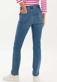Jeans en denim, bleu clair, taille haute avec cinq poches, coupe droite, associés à des baskets blanches, texture lisse et design classique.