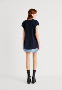 Marineblå t-skjorte med korte ermer og løs passform, sammen med et lyst denim mini-skjørt og svarte helsesko. Enkelt design og myk tekstur.