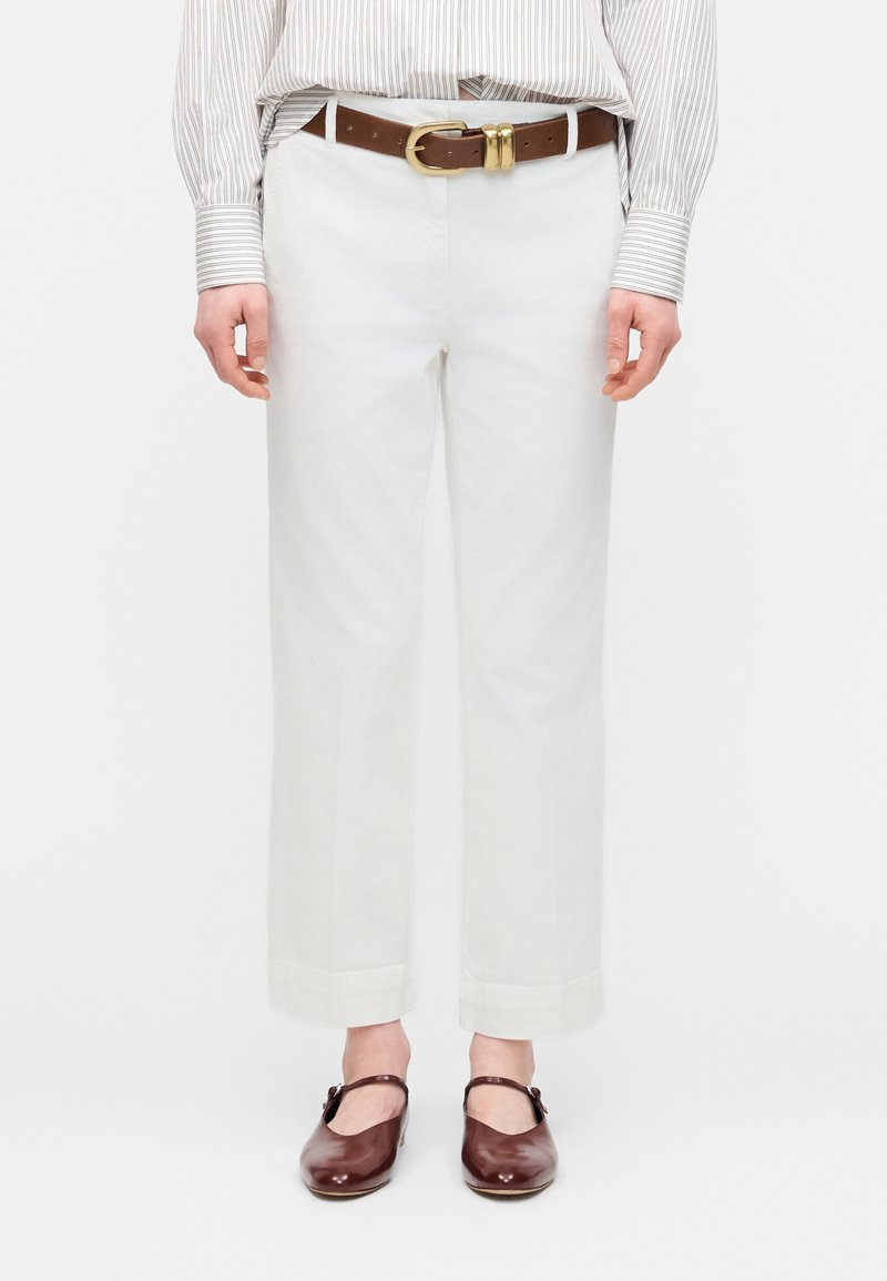 Λευκά cropped παντελόνια με φαρδιά μπατζάκια και διπλωμένες άκρες, σε συνδυασμό με καφέ ζώνη και σκούρα καφέ παπούτσια Mary Jane σε ένα άτομο.