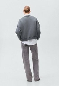 Sivkropecen pulover s dolgimi rokavi, rebrastim robom in sproščenim krojem, v kombinaciji s svetlosivimi hlačami ravnega kroja.