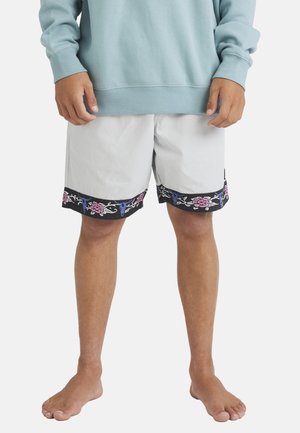 White swim shorts with black floral and skull patterns at the hem, made from lightweight material, paired with a light blue sweatshirt.