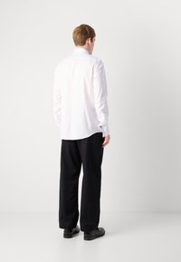 Witte langarmshirt met een spread kraag, rugplooien en ronde zoom, gecombineerd met zwarte geplooide broeken en zwarte schoenen.