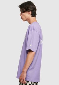 Purple cotton t-shirt with short sleeves, relaxed fit, featuring a graphic detail on the front and a logo near the sleeve. Plain back.
