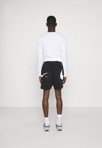 Czarne szorty z białym logo, w połączeniu z białą koszulą z długim rękawem. Szorty posiadają kieszenie i luźny krój, noszone z białymi skarpetkami i trampkami.