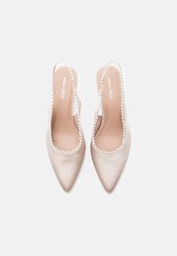 Chaussures slingback en satin beige avec un bout pointu, ornées d'une bordure d'accents en perles le long de l'ouverture. Texture lisse et design minimaliste.