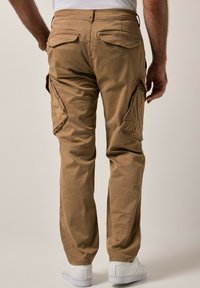 Khakifarbene Cargo-Hosen mit mehreren Taschen, gerader Schnitt, aus weichem Baumwollstoff, kombiniert mit weißen Sneakers, von hinten betrachtet.
