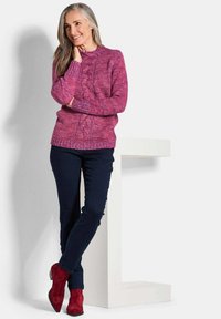 Pull en maille texturé magenta avec un col rond et un détail de torsade, associé à un pantalon bleu foncé et des bottines rouges.