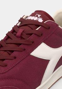 Tenis burgundy din suede, cu un logo din piele albă, având șireturi texturate și un design cu vârf rotund. Talpă din cauciuc cu cusături vizibile.