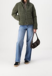 Zelená kordurová péřovka s vysokým límcem, kombinovaná se světle modrými širokými džíny a tmavě hnědou kabelkou. Černé tenisky s hnědým podrážkou.