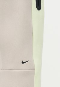 Υφασμάτινα πάνελ σε μπεζ και ανοιχτό πράσινο με μαύρα λογότυπα Nike swoosh στο μπεζ πάνελ και κοντά στη ραφή.