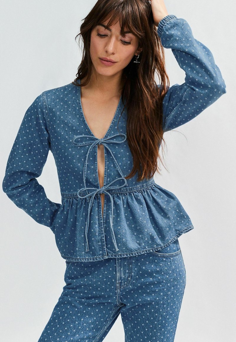 Denim ülemise osa sügava V-kaelusega, nööriga kinnitustega, peplumi äärisega ja valgete täppidega. Pikad varrukad kogutud mansettidega. Kooskõlastatud denimpüksid.