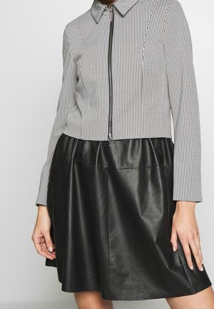 Black leather skirt with a textured, houndstooth patterned cropped jacket featuring a front zipper and collared neckline.
