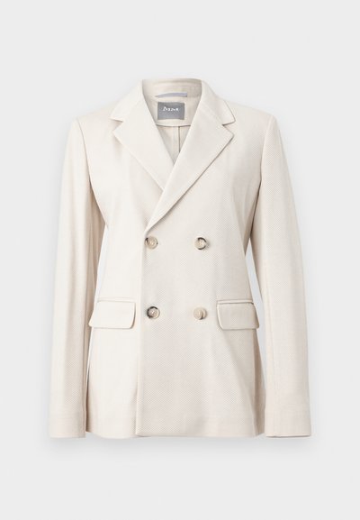 Κρεμ διπλόσπαστο σακάκι με φαρδιές πέτο, τέσσερα κουμπιά, τσέπες με καπάκι και υφασμάτινη υφή, παρουσιασμένο σε απλό φόντο.