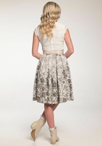 Weißes Spitzen-Crop-Top mit kurzen Ärmeln, kombiniert mit einem knielangen, plissierten Rock mit beigem Blumenmuster und hellen Knöchelstiefeln.