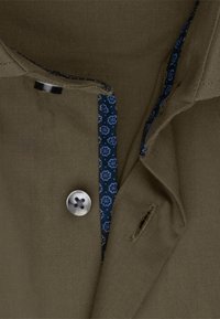Olivengroene shirt met een marineblauw bloemenpatroon aan de binnenkant van de kraag, voorzien van een zilveren knoop en een klein zakdetail aan de voorkant.