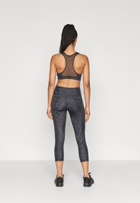 Μαύρο αθλητικό σουτιέν με λεπτομέρειες από δίχτυ και αντίστοιχο κολάν με διακριτικό σχέδιο λεοπάρ. Φορώντας μαύρα αθλητικά παπούτσια.