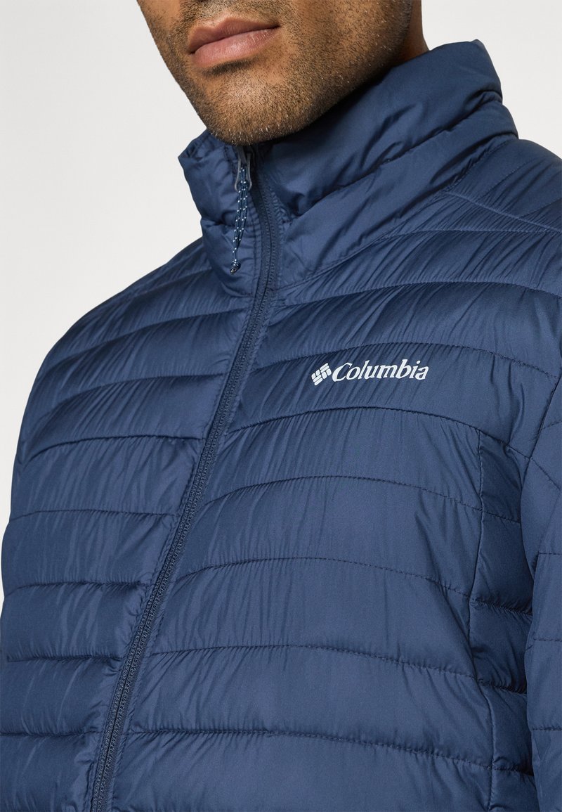 Veste matelassée bleu marine avec col haut et surface subtilement texturée. Dotée d'une fermeture éclair intégrale et du logo Columbia sur la poitrine gauche.