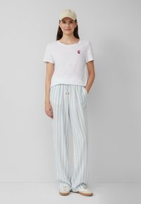 Witte t-shirt met korte mouwen, voorzien van een rood hartontwerp, gecombineerd met lichtblauwe en witte gestreepte wijde broek en beige sneakers.