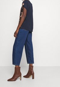 Granatowy top z krótkim rękawem w kontrastowy beżowy wzór w kropki, połączony z luźnymi niebieskimi dżinsami oraz brązowymi skórzanymi botkami na kostkę z blokowym obcasem.