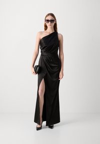 Melnas satīna vakara kleita ar vienu plecu, sānu šķēlumu un vaļīgu drapējumu. Pāris ar mazu melnu somiņu un smailām papēžiem.