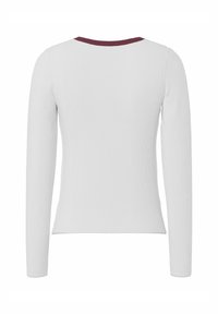 Vit långärmad ribbstickad skjorta med rund halsringning och en mörk bordeauxfärgad kant, sedd bakifrån.