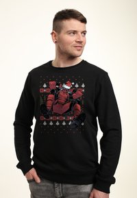 Sudadera negra con un gráfico colorido de un personaje con un gorro de Santa, rodeado de patrones navideños en rojo y blanco.
