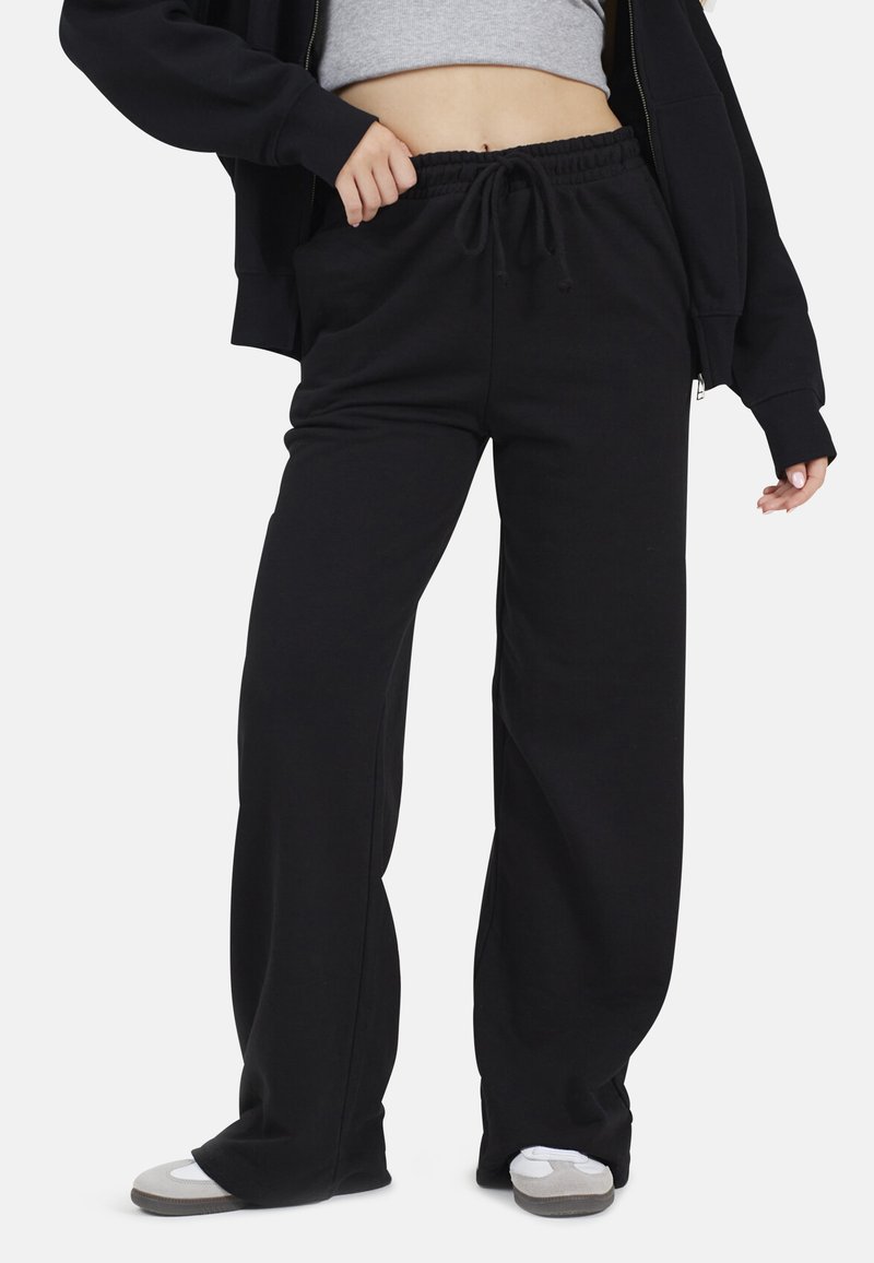 Pantalon de survêtement noir en mélange de coton, présentant une taille élastique avec cordon de serrage, une coupe ample et des poches latérales. Texture lisse.