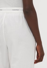 Weiße Hosen mit einem elastischen Bund, gekennzeichnet mit "Calvin Klein." Glattes, leichtes Material. Sichtbare seitliche Taschen. Lässiger Schnitt.
