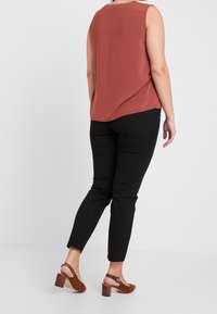 Roestkleurig mouwloos topje, zwarte slim-fit broek en bruine hakken met een gestructureerde band. Glad materiaal, minimalistisch ontwerp.