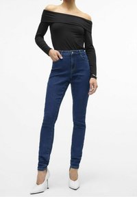 Musta olkaimeton paita yhdistettynä korkeavyötäröisiin sinisiin skinny-farkkuihin ja valkoisiin kärkipohjaisiin korkokenkiin. Silkkinen kangas, kapea malli ja siistit linjat.