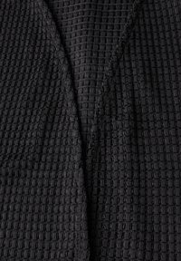 Czarna, teksturowana tkanina z wzorem w kratkę, o lekkiej, tkanej strukturze i otwartym dekolcie. Idealna do noszenia w warstwach lub na co dzień.