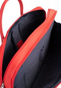 Rode gestructureerde tas met een gladde synthetische buitenkant, open bovenkant die een donkere stoffen binnenkant onthult, met meerdere vakken voor organisatie.