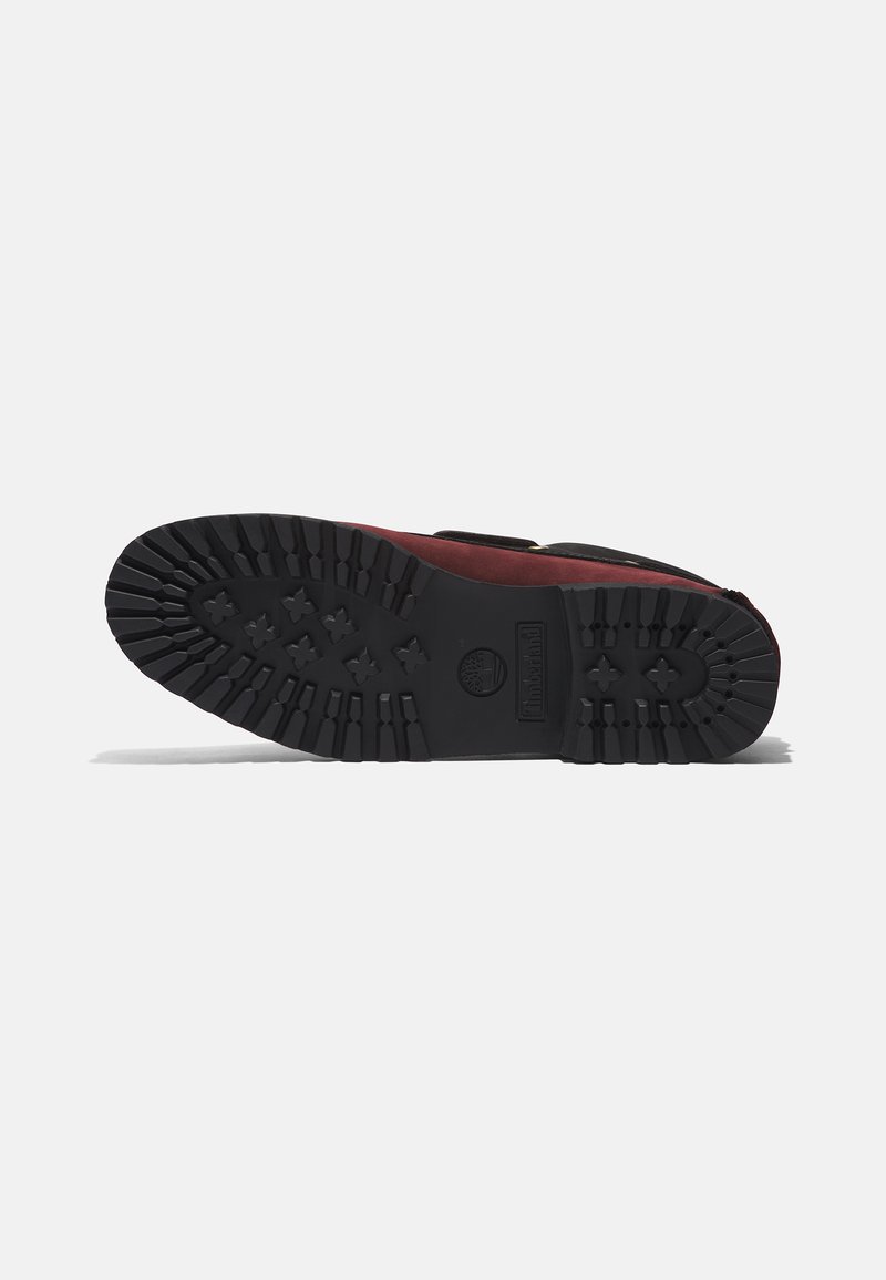 Suela de bota Timberland, de goma negra con un diseño de dibujo profundo, que presenta patrones elevados y logo, diseñada para ofrecer tracción en diversas superficies.