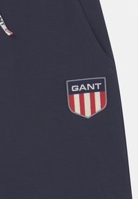 Dunkelblaues Sweatshirt mit einem gestickten GANT-Logopatch im Schilddesign, das rote und weiße Streifen integriert. Aus weichem Baumwollmaterial.