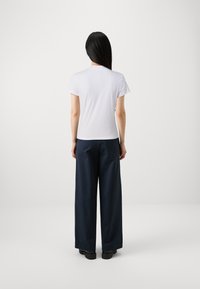 T-shirt bianca a maniche corte con scollo rotondo, abbinata a pantaloni larghi blu navy e scarpe nere, vista da dietro.