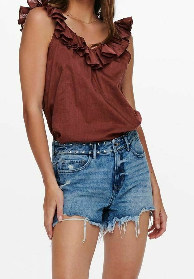 Femme portant un haut marron sans manches à volants, associé à un short en denim bleu déchiré taille haute avec une ceinture cloutée.