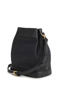 Crna i siva filcasta torba u obliku kante s kožnim detaljima, metalnim kopčom i podesivim remenom. Ima mekanu teksturu i strukturirani oblik.