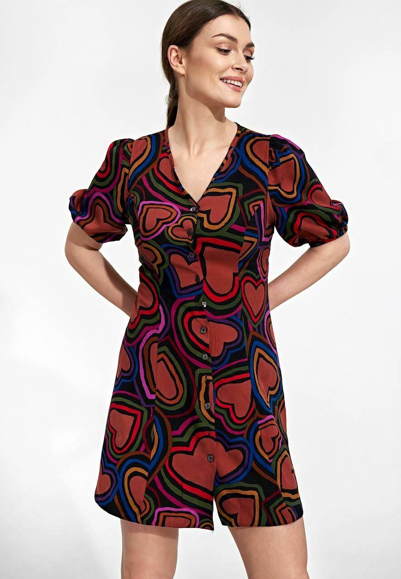 Kurzes Kleid mit einem mehrfarbigen Herzmuster auf schwarzem Hintergrund. Hergestellt aus einem glatten Stoff mit einem V-Ausschnitt und Knopfverschluss.