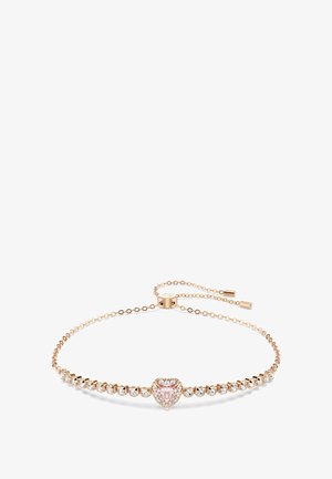 Bransoletka w kształcie serca z różowym kamieniem pośrodku, otoczona przez przezroczyste kryształy, na delikatnym łańcuszku w różowym złocie z regulowanym zapięciem.