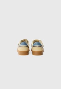 Zapatillas beiges con acentos azules, materiales de cuero y goma, punta redonda y suela de goma color marrón claro. Marca visible en el talón.