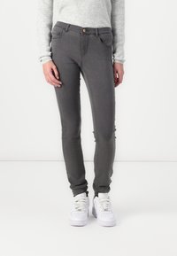 Grå slim jeans med hög midja, med framfickor och knäppning. Bärs med vita sneakers och en ljus tröja.